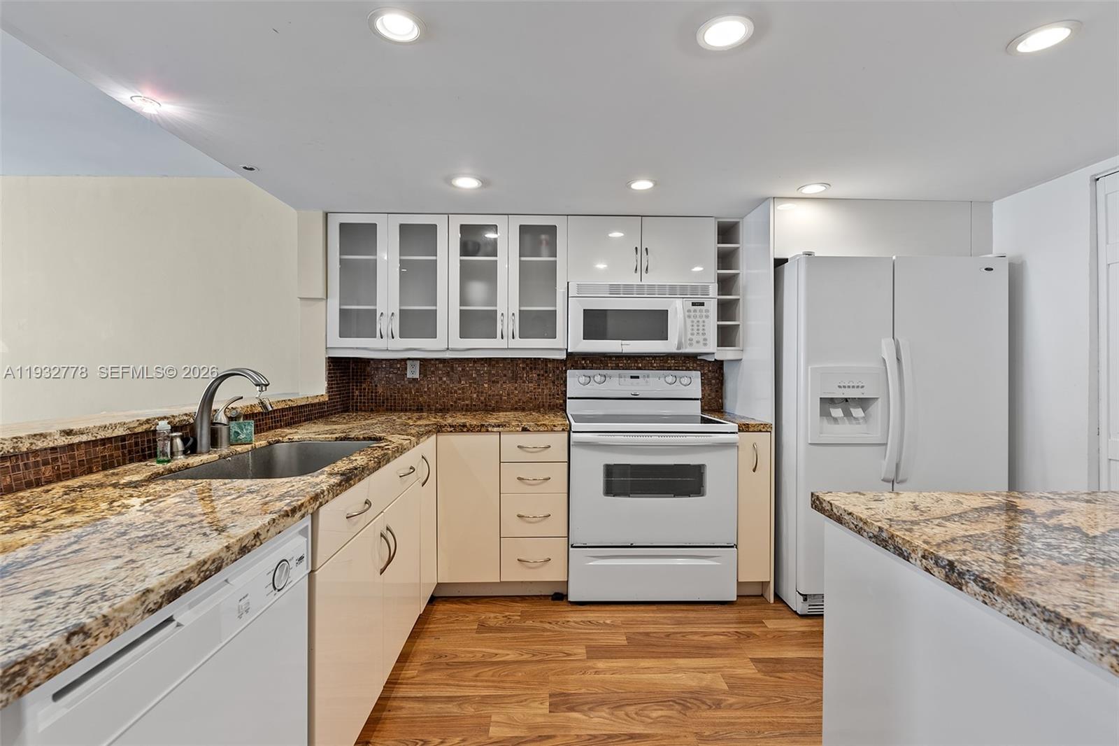 A kitchen features white cabinetry, granite countertops, a tiled backsplash, and white appliances — 555 NE 15th St # 14G, Miami FL 33132, MIAMI, FL