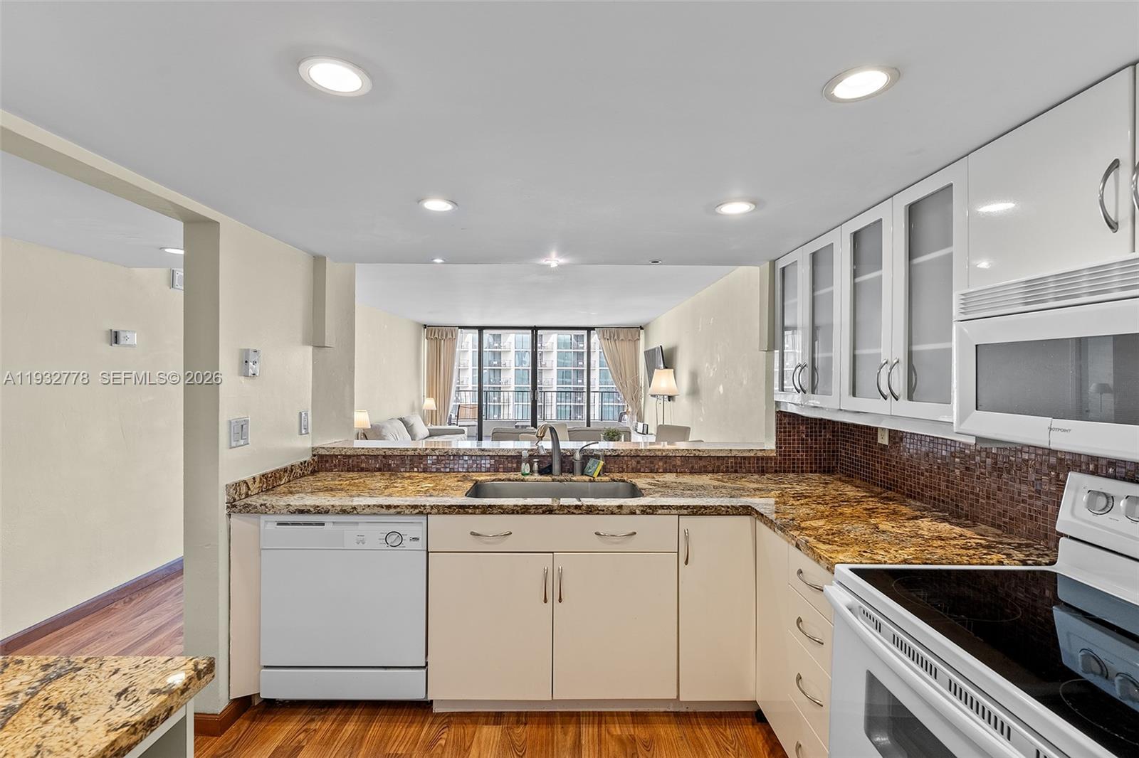 A kitchen features granite countertops, white cabinetry, and a pass-through window overlooking the living area — 555 NE 15th St # 14G, Miami FL 33132, MIAMI, FL