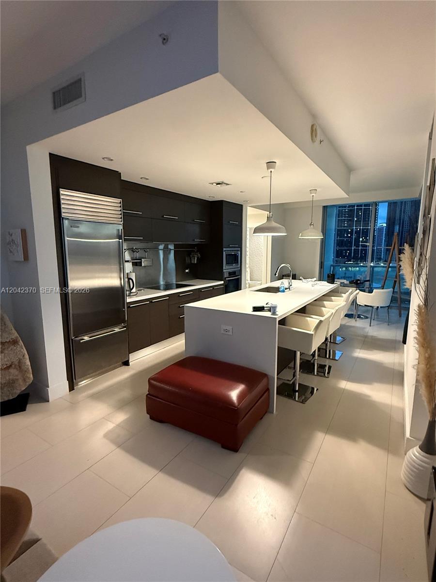 A modern kitchen features dark cabinetry, a white island with bar seating, and stainless appliances — 900 Biscayne Blvd # 2312, Miami FL 33132, MIAMI, FL