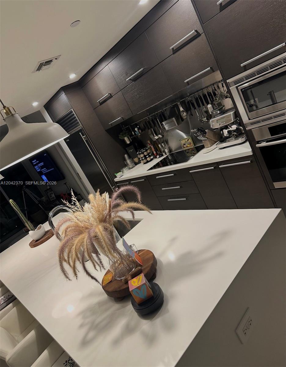 A modern kitchen features dark wood cabinetry, white countertops, and a large central island — 900 Biscayne Blvd # 2312, Miami FL 33132, MIAMI, FL