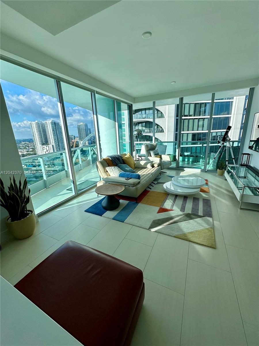 A modern living room features floor-to-ceiling windows, a colorful area rug, and city views — 900 Biscayne Blvd # 2312, Miami FL 33132, MIAMI, FL