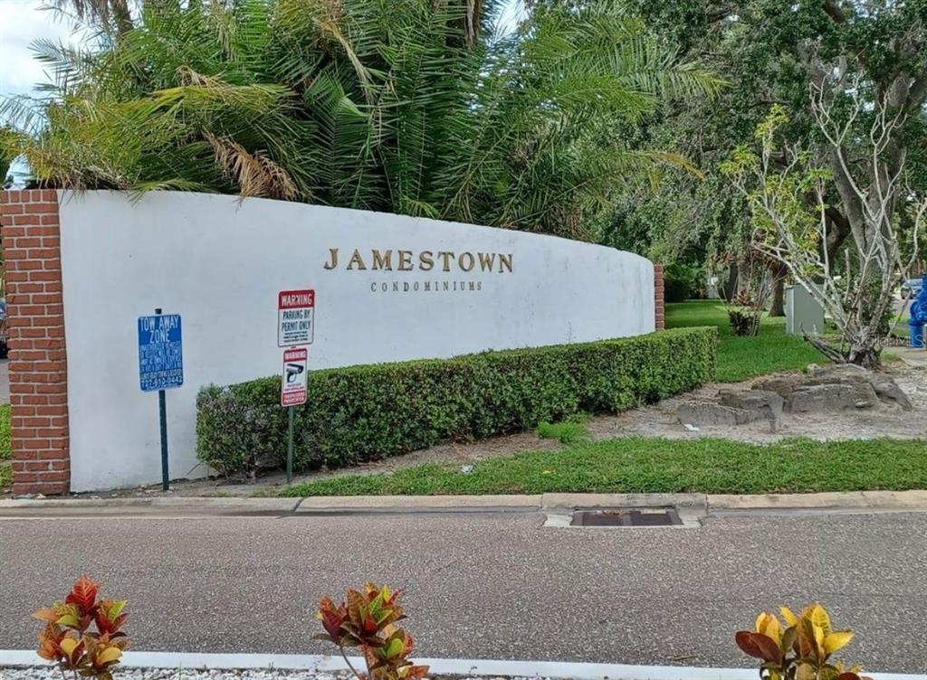 A white curved wall with the Jamestown Condominiums sign stands beside a road and landscaping — 1131 84TH AVENUE N UNIT D, ST PETERSBURG, FL