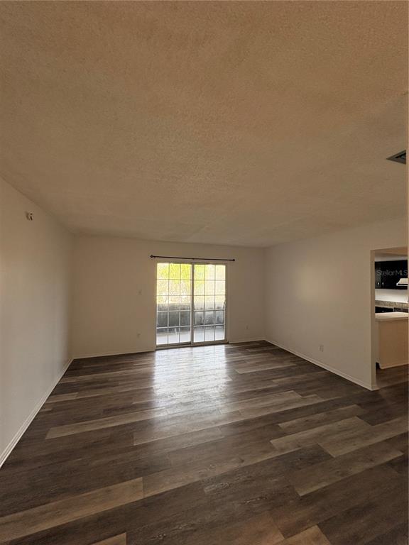 An empty living room features wood-look flooring, white walls, and a sliding glass door — 1131 84TH AVENUE N UNIT D, ST PETERSBURG, FL