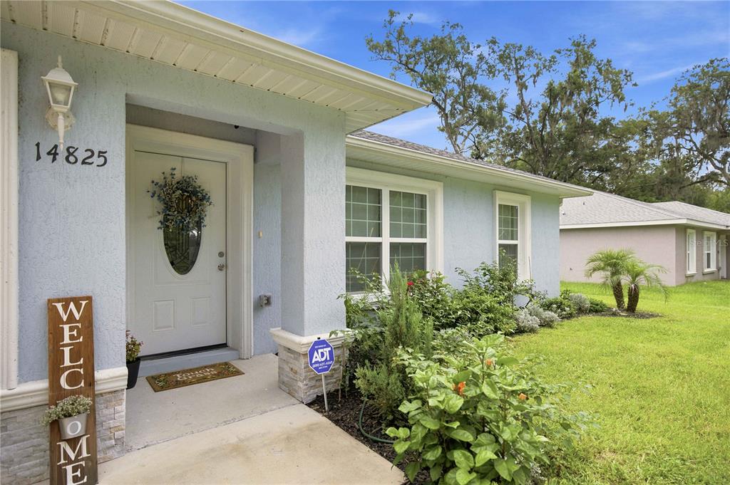 The exterior of a light blue house features a front porch, white door, and landscaping — 14825 SE 28TH TERRACE, SUMMERFIELD, FL