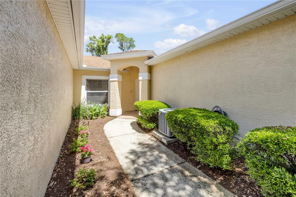 A concrete walkway leads to the front entrance of a house with beige stucco walls — 132 TURNBULL VILLAS CIRCLE, NEW SMYRNA BEACH, FL