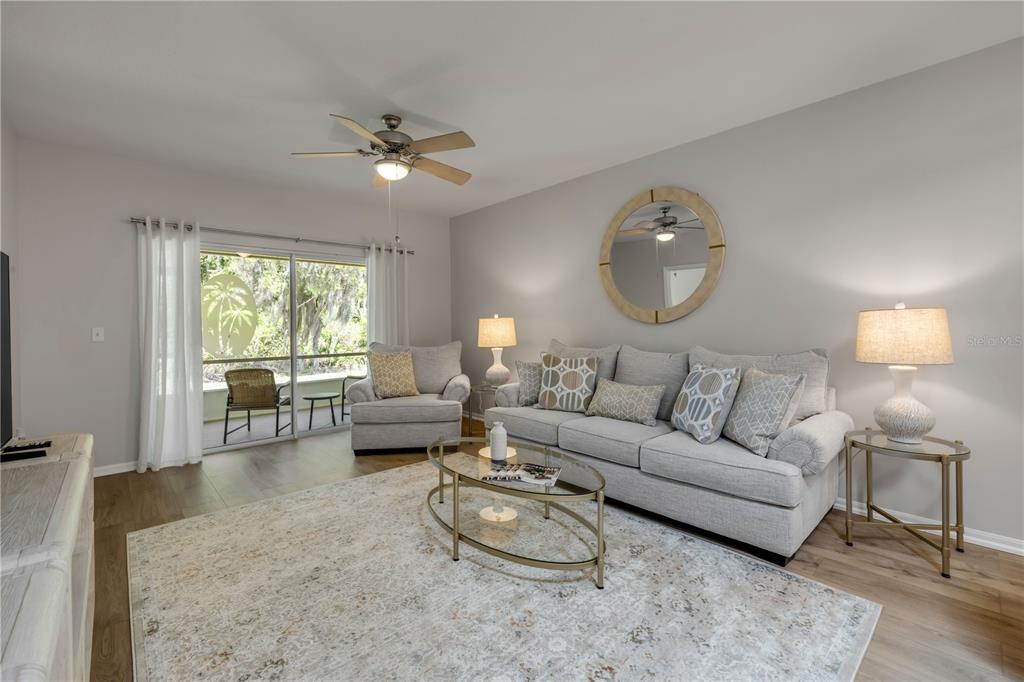 A living room features a gray sofa, matching armchair, glass coffee table, and sliding glass doors — 132 TURNBULL VILLAS CIRCLE, NEW SMYRNA BEACH, FL