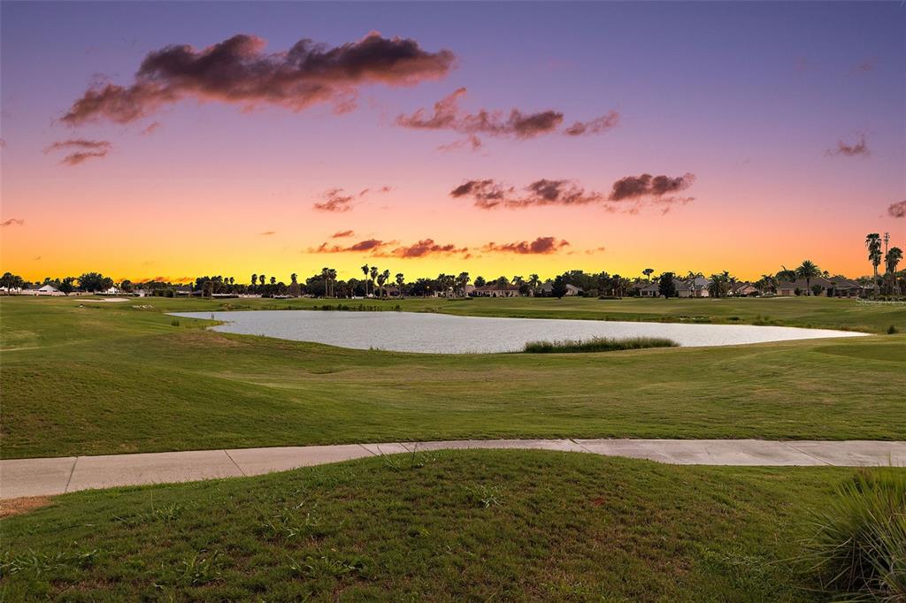 A view of a golf course pond at sunset with a paved path in the foreground — 2216 BLACKVILLE DRIVE, THE VILLAGES, FL