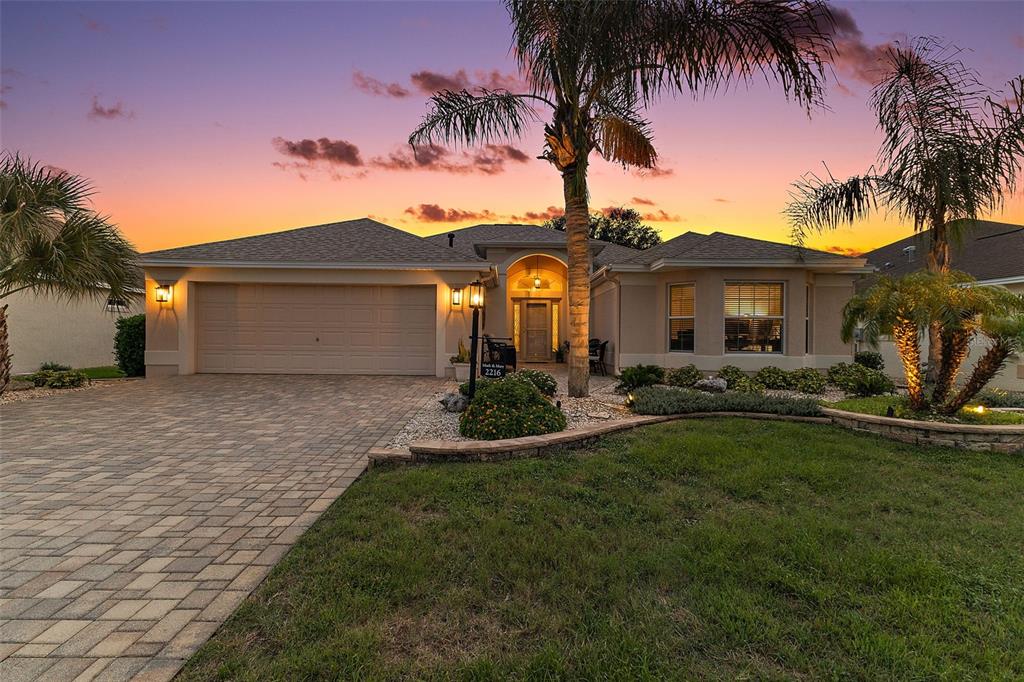 A single-story house with a paved driveway, palm trees, and a sunset sky — 2216 BLACKVILLE DRIVE, THE VILLAGES, FL