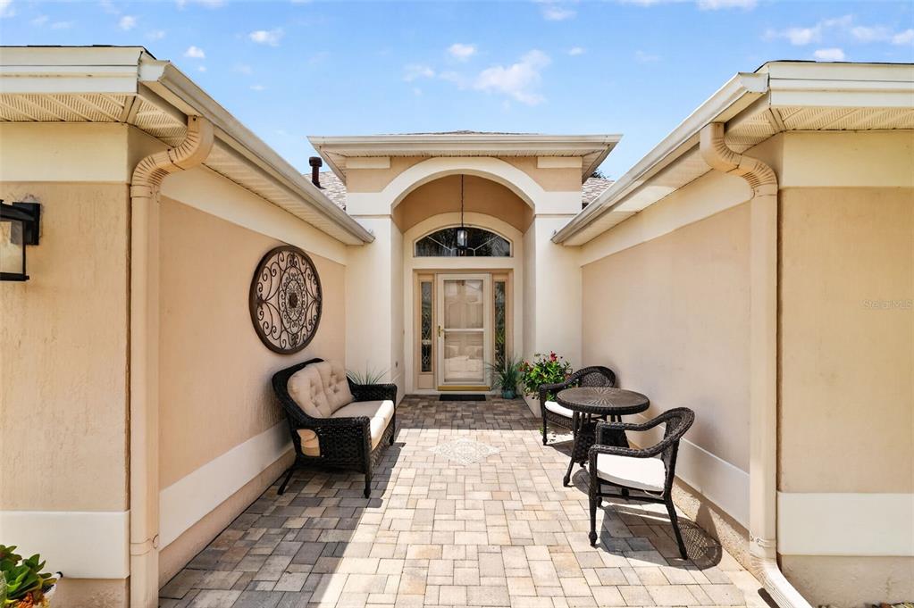 A paved courtyard entrance features a wicker sofa, two chairs, a table, and a front door — 2216 BLACKVILLE DRIVE, THE VILLAGES, FL