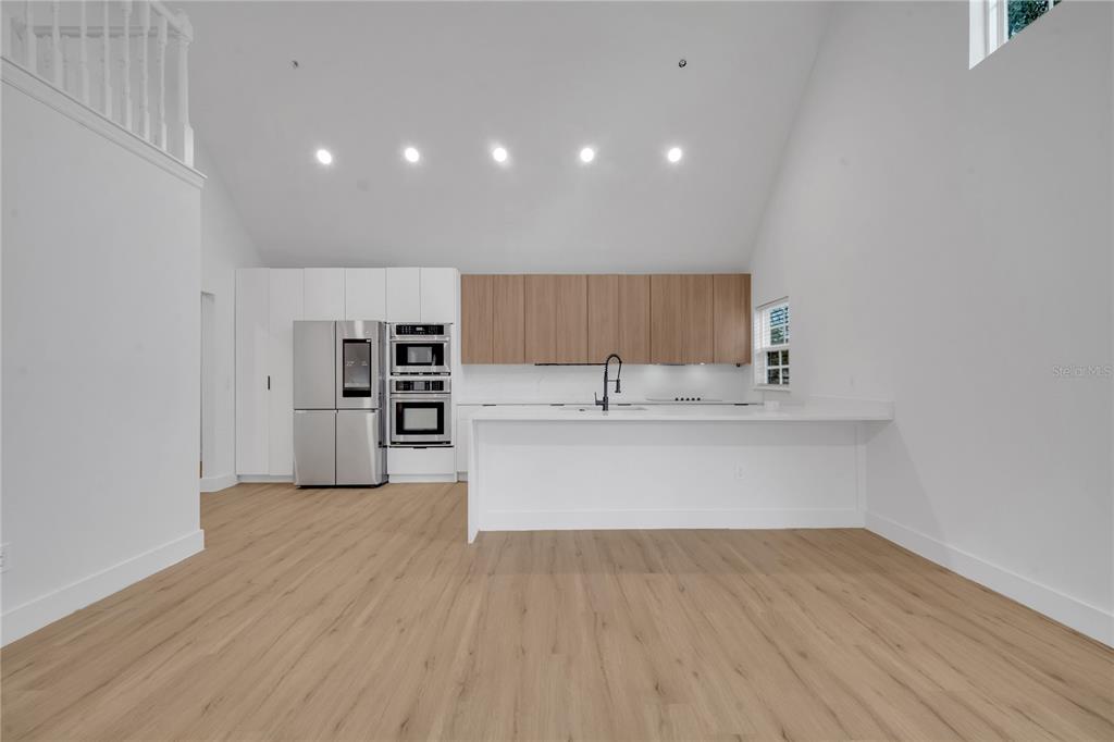 A modern kitchen features white cabinetry, wood-toned upper cabinets, stainless steel appliances, and light flooring — 6593 QUEENS BOROUGH AVENUE UNIT 202, ORLANDO, FL