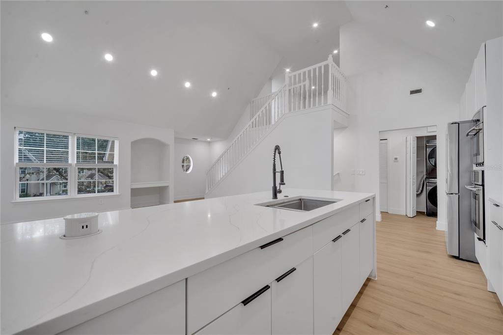 A modern kitchen features a large white quartz island, white cabinetry, and a staircase nearby — 6593 QUEENS BOROUGH AVENUE UNIT 202, ORLANDO, FL