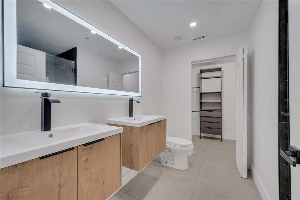 A modern bathroom features dual floating wood vanities, black faucets, and a large illuminated mirror — 6593 QUEENS BOROUGH AVENUE UNIT 202, ORLANDO, FL