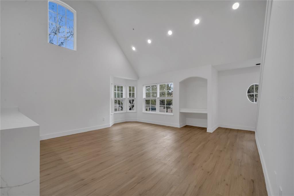 A bright, empty living room features vaulted ceilings, light wood floors, and a built-in alcove — 6593 QUEENS BOROUGH AVENUE UNIT 202, ORLANDO, FL