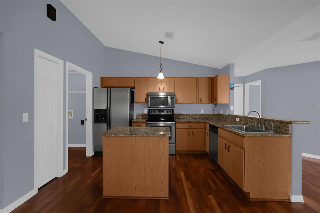 A kitchen features wood cabinets, granite countertops, stainless steel appliances, and a central island — 1147 NORMANDY DRIVE, KISSIMMEE, FL
