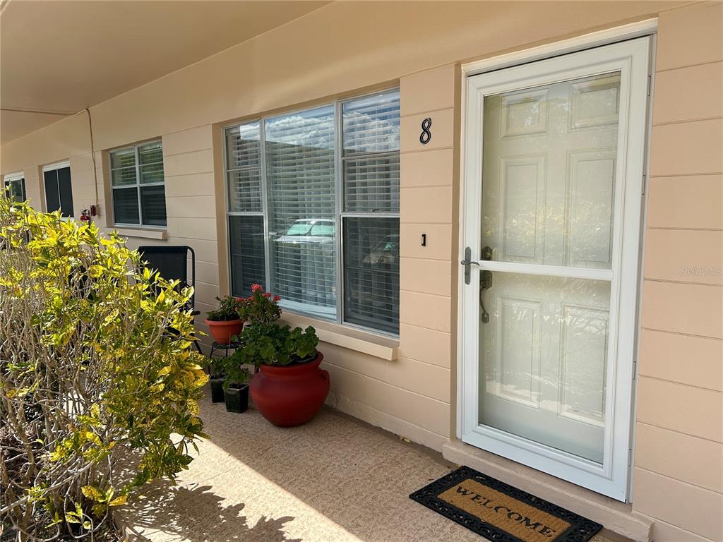 The exterior of a beige building features a front door, a window, and potted plants — 2286 NORWEGIAN DRIVE UNIT 8, CLEARWATER, FL