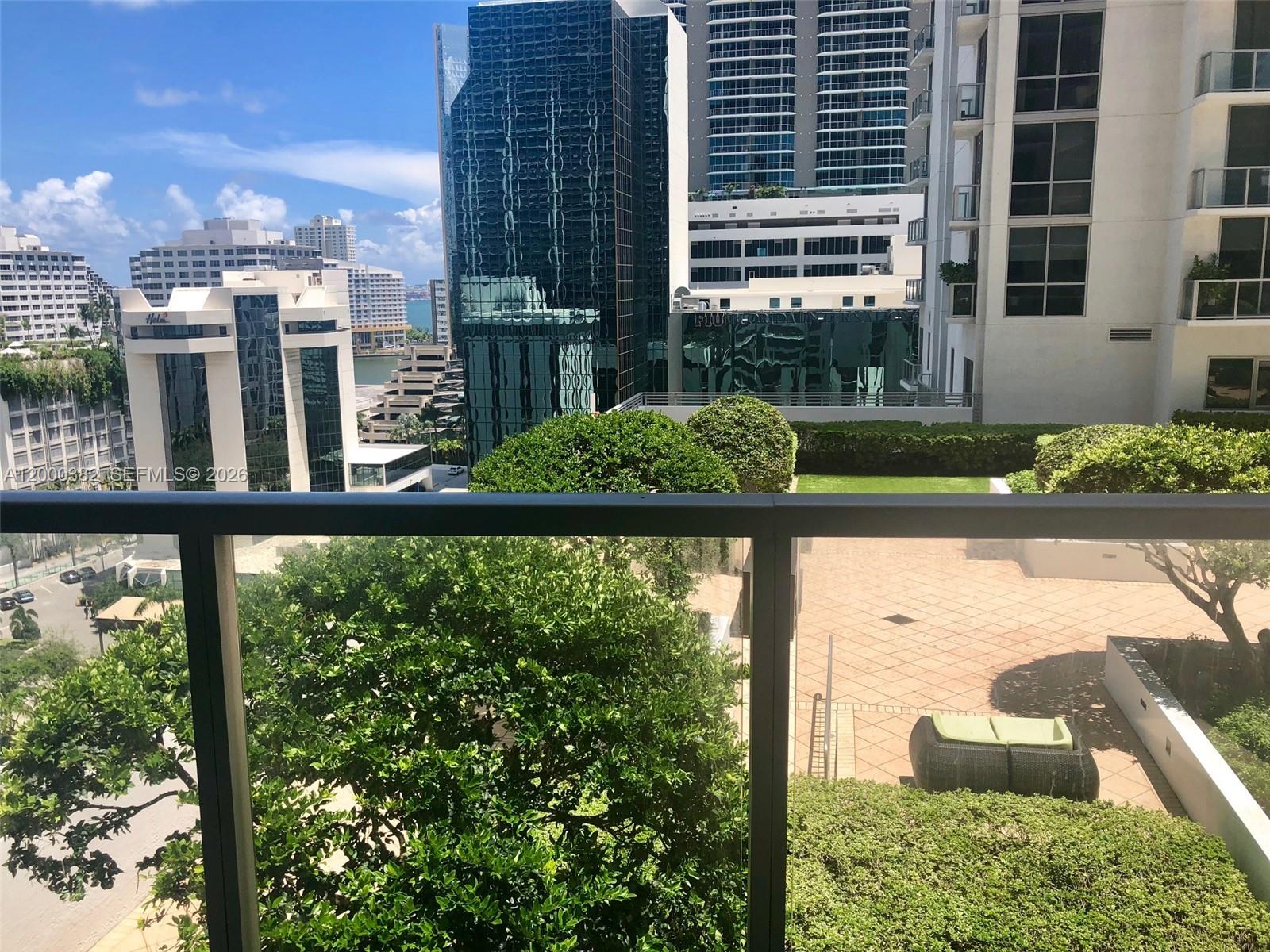 A balcony view overlooks a landscaped terrace, nearby modern buildings, and a distant cityscape — 1050 BRICKELL AV # 1408, Miami FL 33131, MIAMI, FL