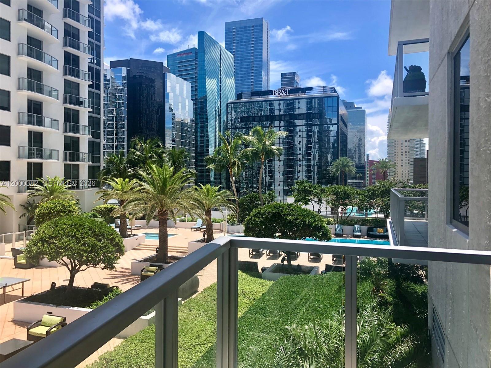 A balcony overlooks a landscaped pool deck surrounded by modern high-rise buildings — 1050 BRICKELL AV # 1408, Miami FL 33131, MIAMI, FL
