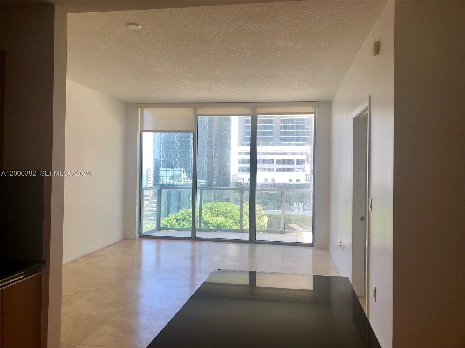 An empty living room features light tile flooring, floor-to-ceiling windows, and a balcony view — 1050 BRICKELL AV # 1408, Miami FL 33131, MIAMI, FL