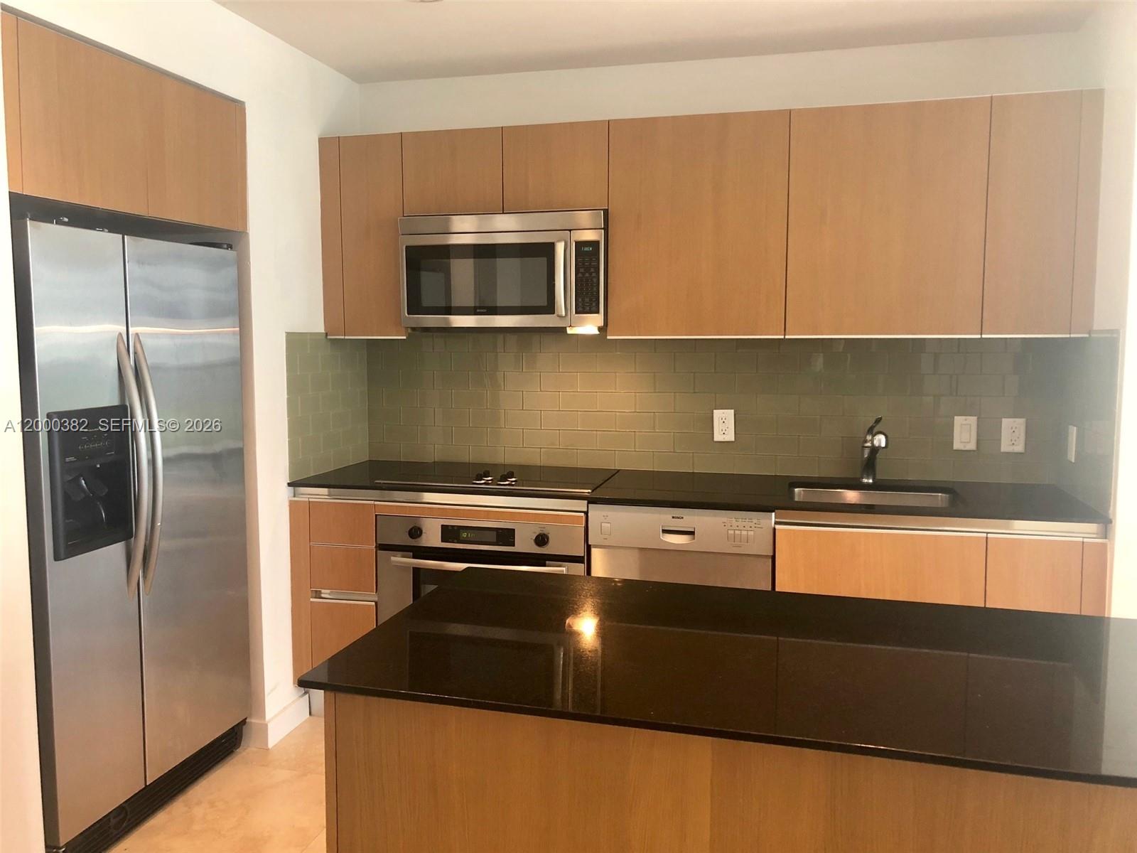 A kitchen features wood cabinets, stainless steel appliances, a black countertop, and a green backsplash — 1050 BRICKELL AV # 1408, Miami FL 33131, MIAMI, FL