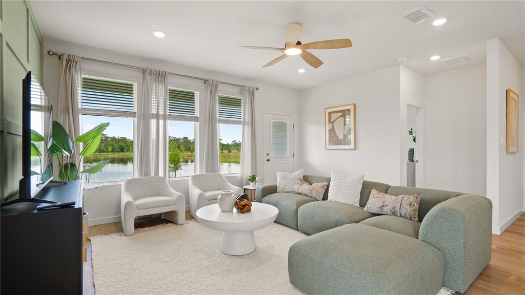 A living room features a green sectional sofa, two armchairs, and windows overlooking a lake — 5120 FLAXLEAF STREET, ST CLOUD, FL