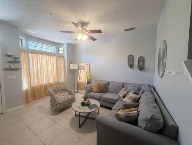 A living room features a grey sectional sofa, a patterned armchair, and a round coffee table — 6013 SCOTCHWOOD GLEN UNIT 17, ORLANDO, FL