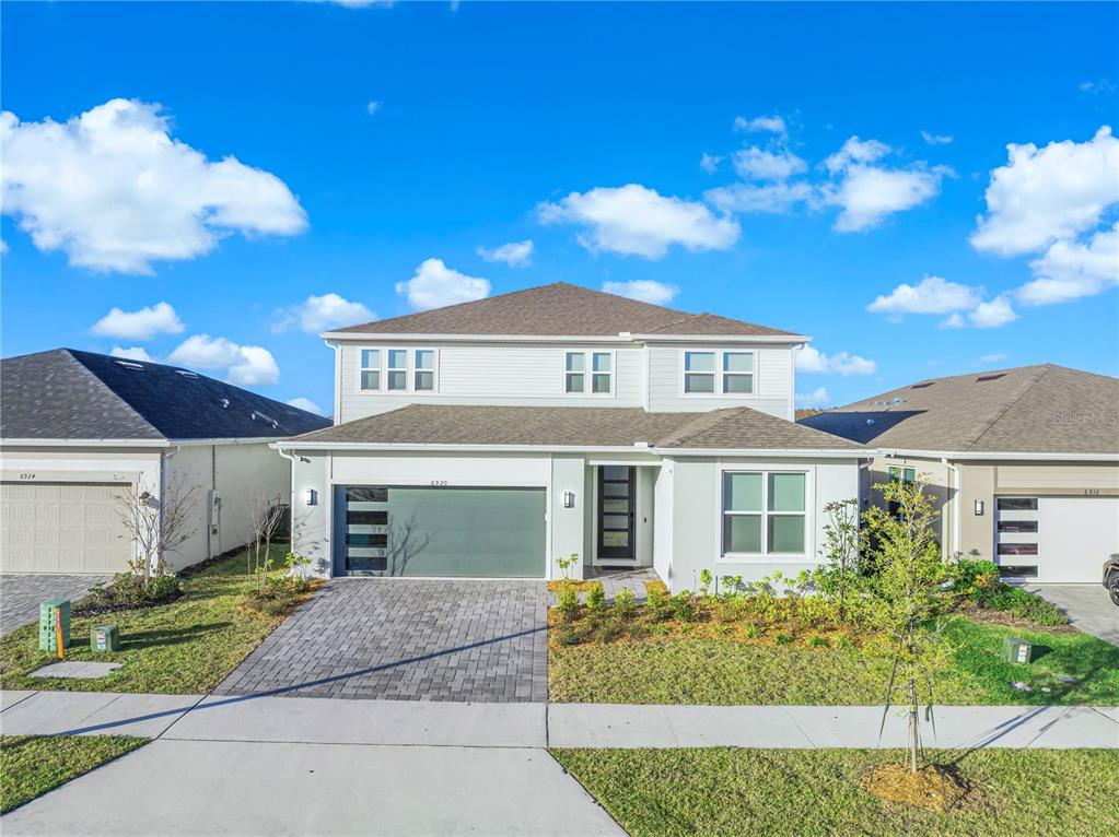 A two-story suburban house with a gray garage, light siding, and a paved driveway — 6920 ROSY SKY AVENUE, ORLANDO, FL