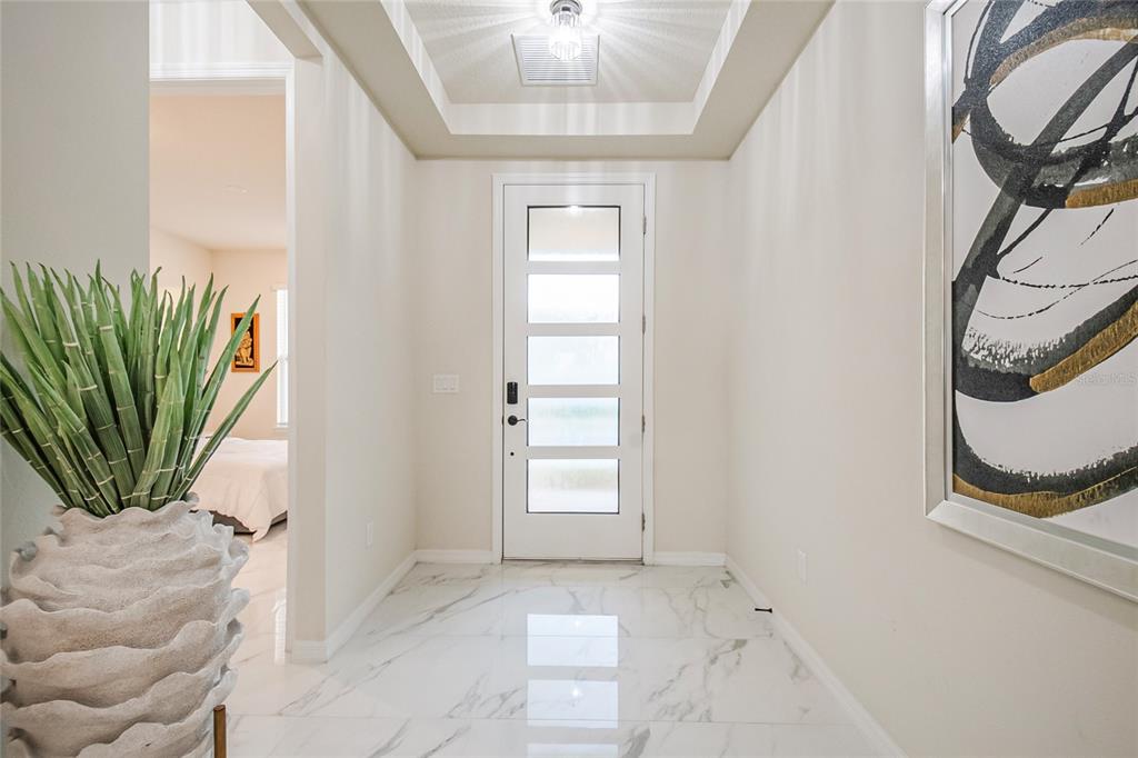 A bright entryway features white marble flooring, a modern front door, and a tray ceiling — 6920 ROSY SKY AVENUE, ORLANDO, FL