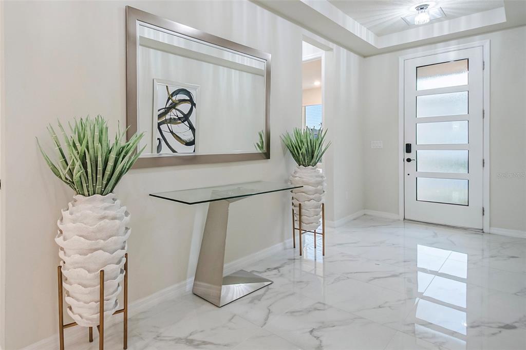 A modern entryway features a glass console table, a large mirror, and two potted plants — 6920 ROSY SKY AVENUE, ORLANDO, FL
