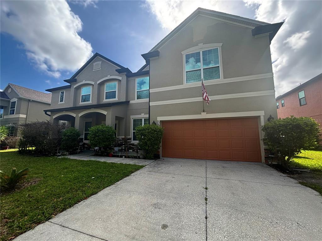 A two-story suburban house with a tan stucco exterior and an orange two-car garage — 3795 MARIETTA WAY, ST CLOUD, FL