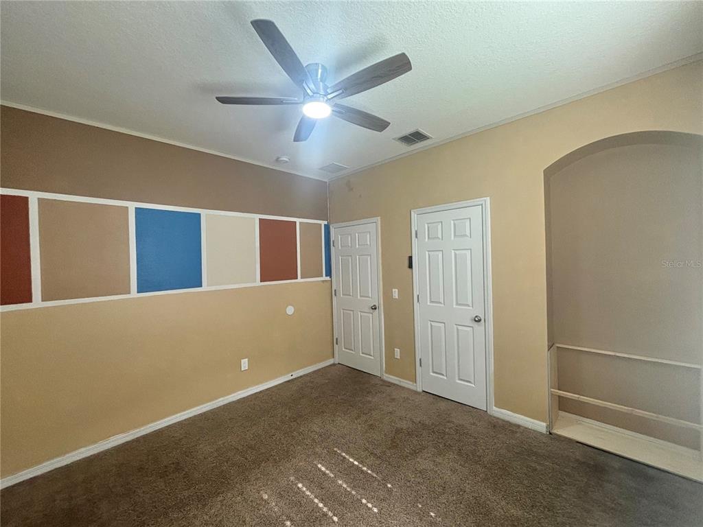 A bedroom features tan walls, a ceiling fan, carpeted flooring, and a decorative wall accent — 3795 MARIETTA WAY, ST CLOUD, FL
