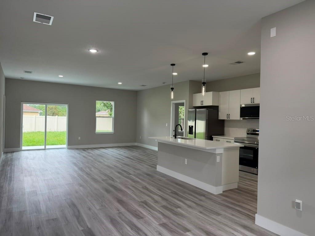An open-concept kitchen and living area features gray walls, wood-look flooring, and a white island — 8089 N MALTESE DRIVE, DUNNELLON, FL