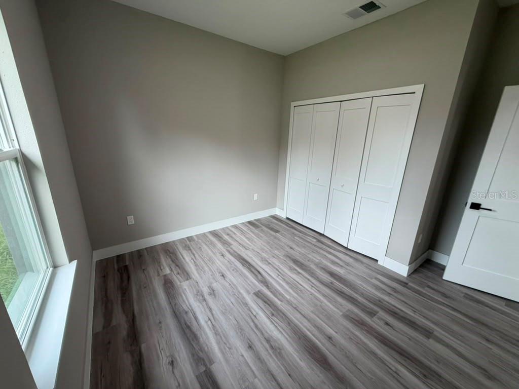 An empty bedroom features light gray walls, wood-look flooring, and white bi-fold closet doors — 8089 N MALTESE DRIVE, DUNNELLON, FL