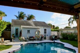 A backyard swimming pool sits in front of a light blue house with a patio — 237 Wenonah Place, West Palm Beach FL 33405, WEST PALM BEACH, FL