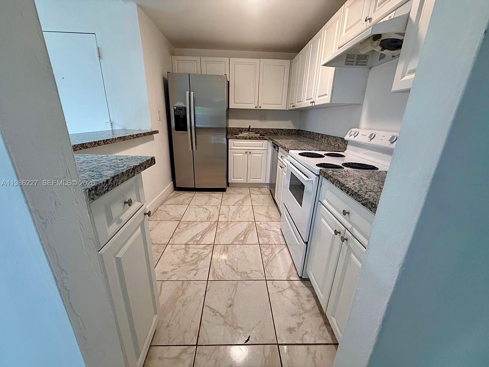 A galley kitchen features white cabinets, granite countertops, stainless steel appliances, and tiled flooring — 10393 N Kendall Dr # U7, Miami FL 33176, MIAMI, FL