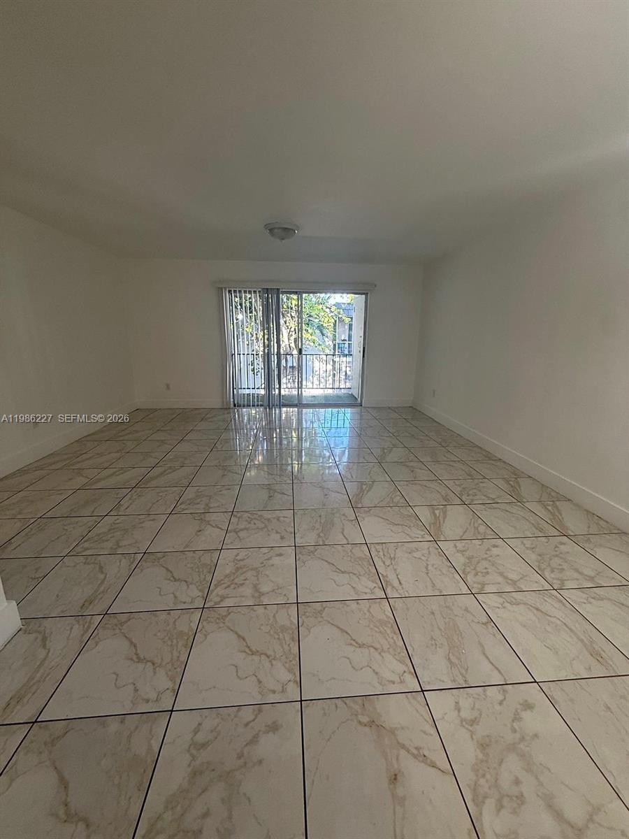 An empty living room features white walls, light-colored marble-style tile flooring, and a sliding glass door — 10393 N Kendall Dr # U7, Miami FL 33176, MIAMI, FL