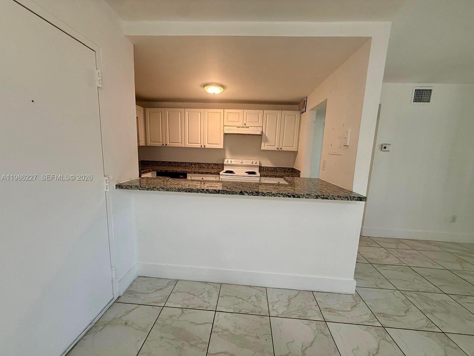 A kitchen with white cabinets and granite countertops overlooks a tiled living area — 10393 N Kendall Dr # U7, Miami FL 33176, MIAMI, FL