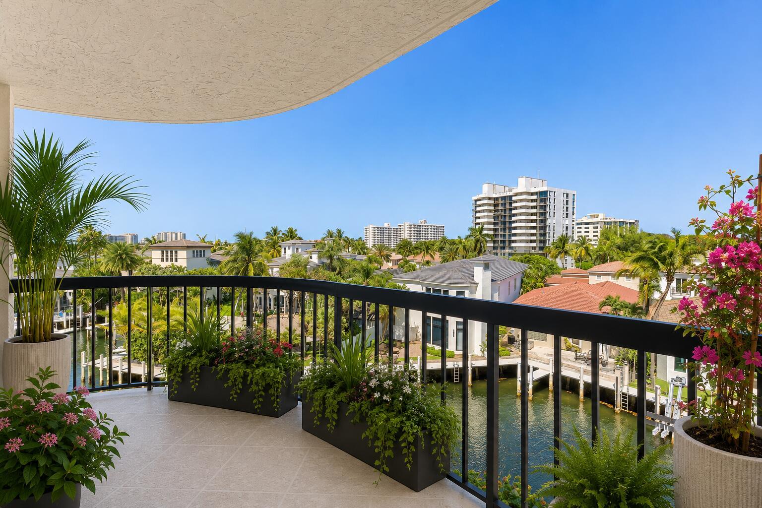 A balcony with potted plants overlooks a canal, residential homes, and distant high-rise buildings — 4740 S Ocean Boulevard S # 501, Highland Beach FL 33487, HIGHLAND BEACH, FL