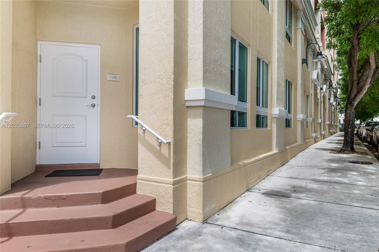 A white door with steps and a handrail sits beside a tan building exterior — 7375 SW 90th St, Miami FL 33156, MIAMI, FL