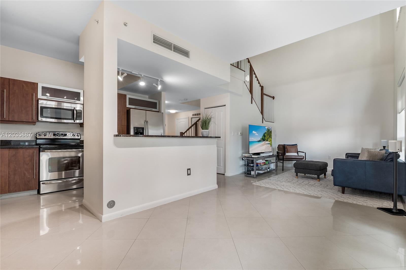 A kitchen with stainless steel appliances opens into a living area with a staircase — 7375 SW 90th St, Miami FL 33156, MIAMI, FL