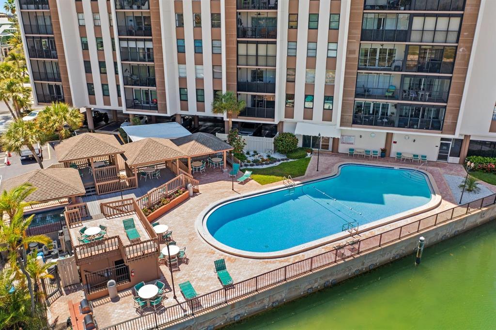 An aerial view shows a swimming pool and patio area adjacent to a multi-story building — 10355 PARADISE BOULEVARD UNIT 812, TREASURE ISLAND, FL