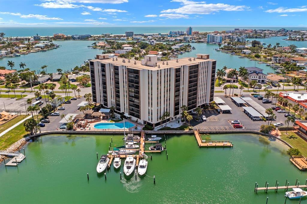 An aerial view shows a multi-story apartment building with a pool and boat docks — 10355 PARADISE BOULEVARD UNIT 812, TREASURE ISLAND, FL