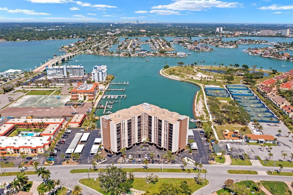 An aerial view shows a multi-story apartment building surrounded by parking, tennis courts, and water — 10355 PARADISE BOULEVARD UNIT 812, TREASURE ISLAND, FL
