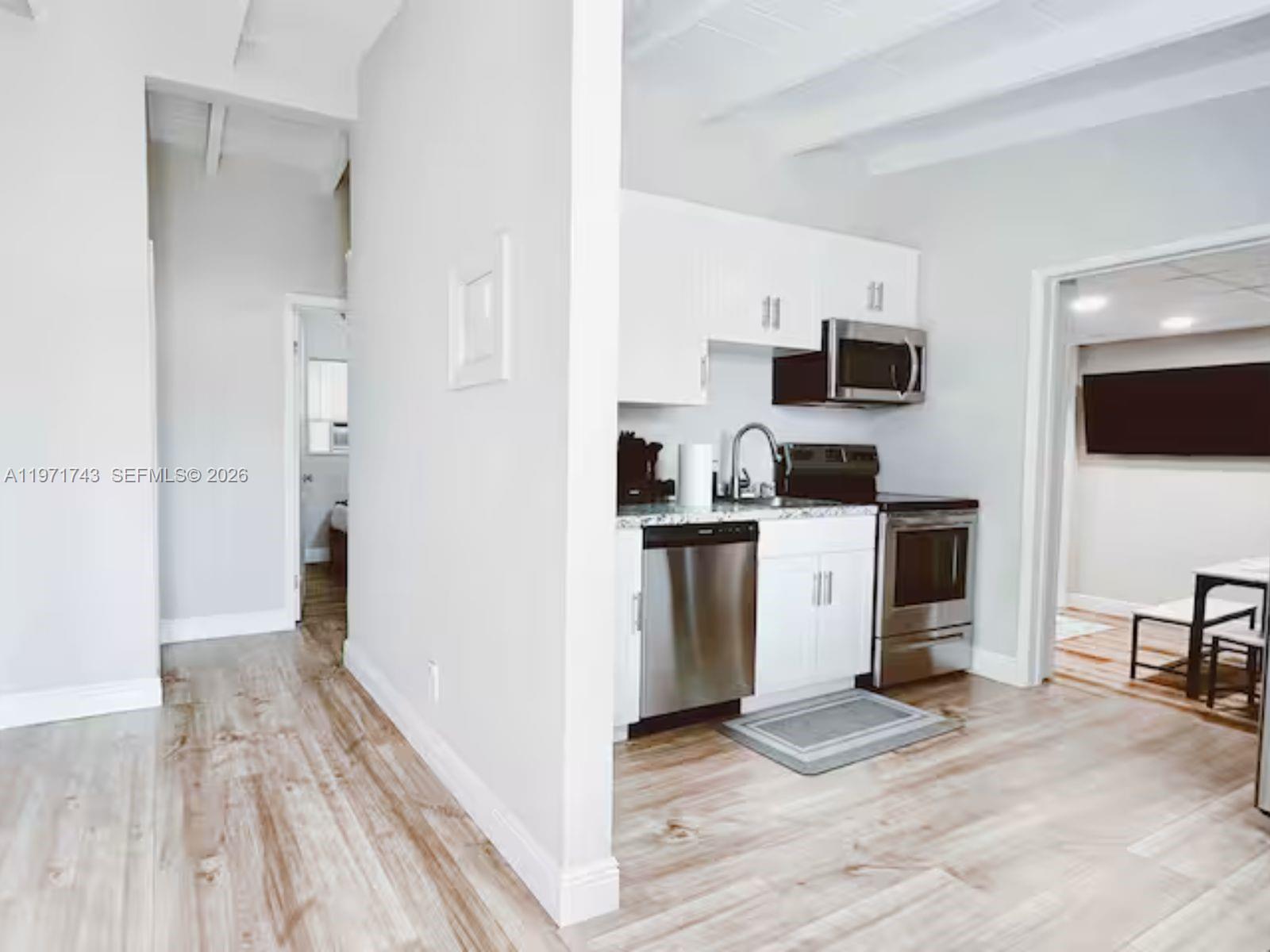 A small kitchen features white cabinets, stainless steel appliances, and light wood-look flooring — 308 NE 8th Ct # 0, Pompano Beach FL 33060, POMPANO BEACH, FL