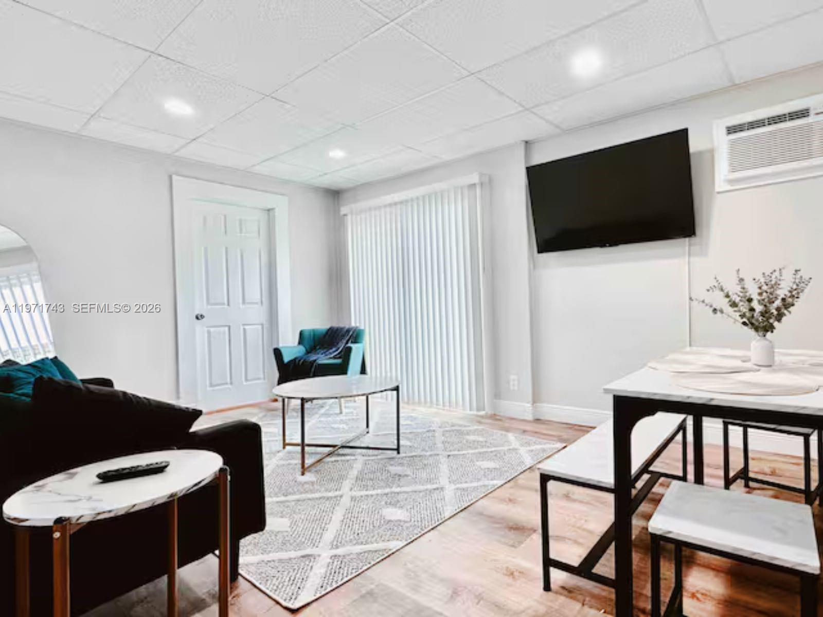 A living and dining area features a drop ceiling, white walls, and wood-look flooring — 308 NE 8th Ct # 0, Pompano Beach FL 33060, POMPANO BEACH, FL