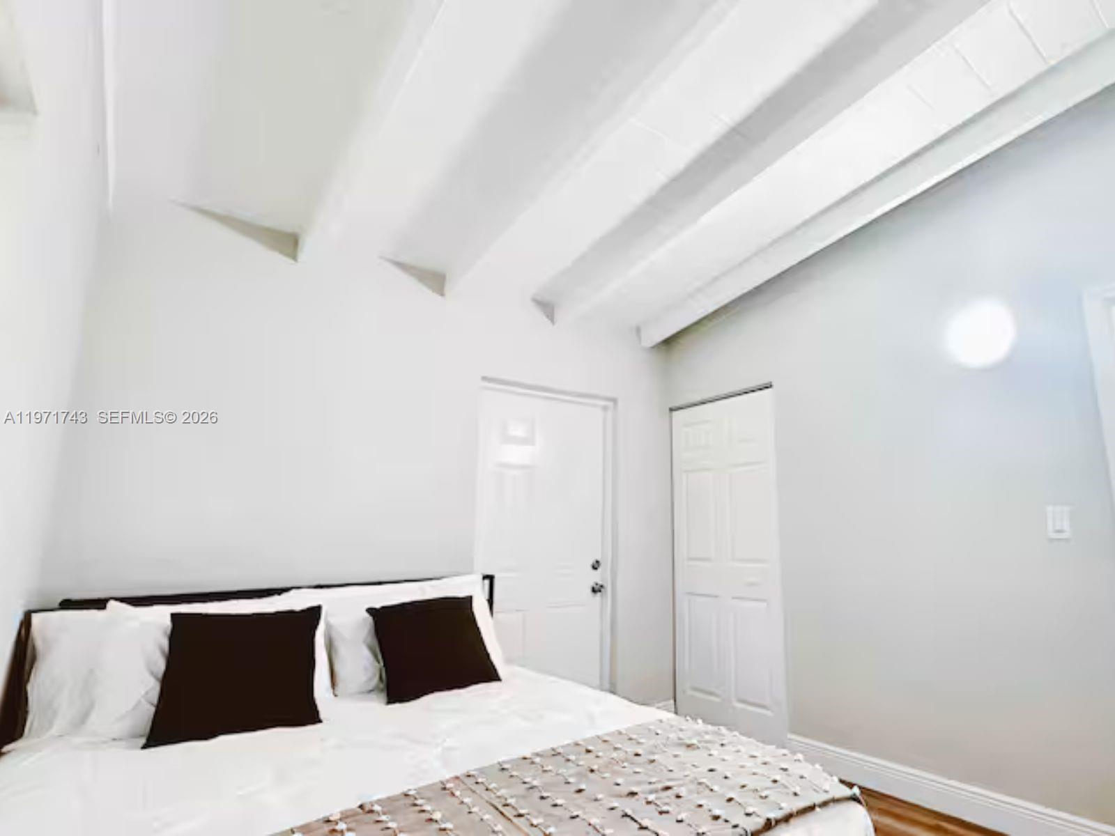 A bedroom features a bed with dark pillows, white walls, and a vaulted beamed ceiling — 308 NE 8th Ct # 0, Pompano Beach FL 33060, POMPANO BEACH, FL
