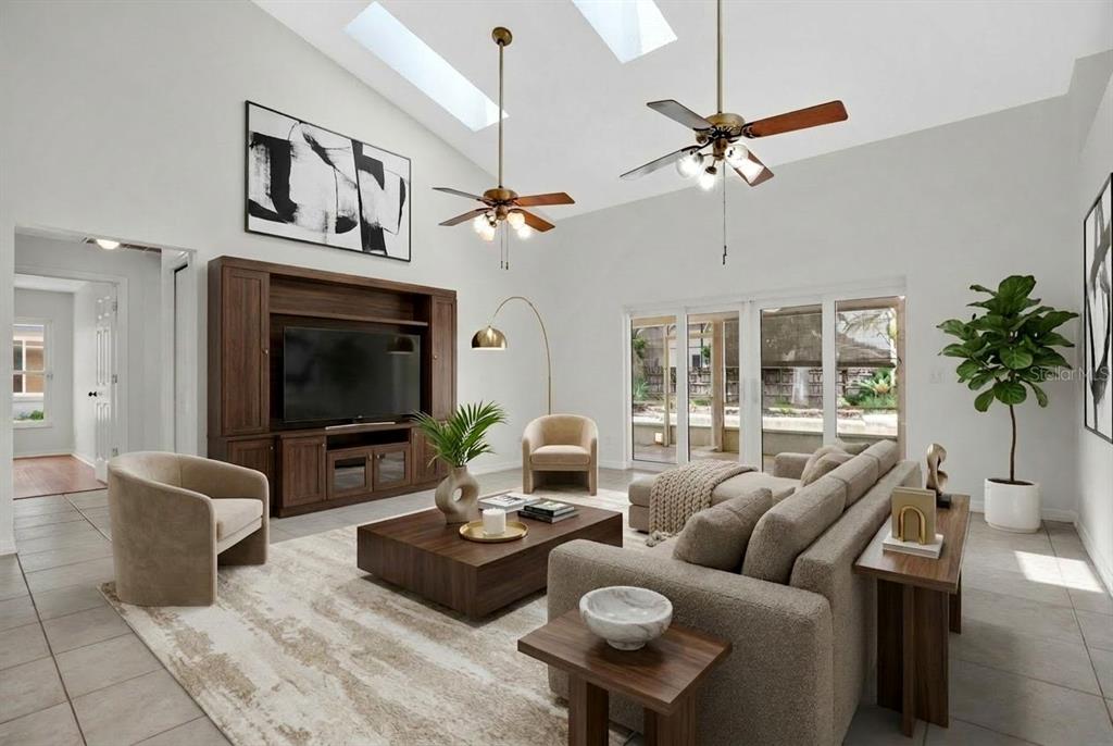 A living room with vaulted ceilings, skylights, a large media console, and neutral furniture — 3886 KINGSTON OAKS COVE, OVIEDO, FL