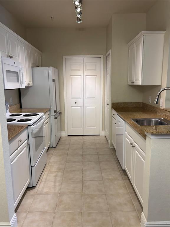 A galley kitchen features white cabinets, granite countertops, and white appliances — 143 SOUTHERN PECAN CIRCLE UNIT 206, WINTER GARDEN, FL