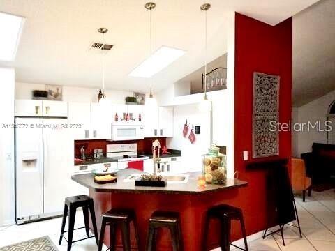 A kitchen features white cabinets, a red accent wall, and a breakfast bar with stools — 11859 HARTFORDSHIRE WAY, ORLANDO, FL