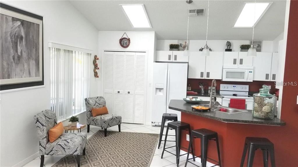 A kitchen with white cabinets, a red breakfast bar, and a seating area with chairs — 11859 HARTFORDSHIRE WAY, ORLANDO, FL