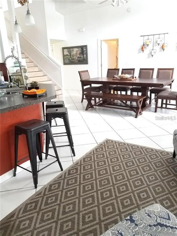 A dining area and kitchen island with bar stools sit on a tiled floor — 11859 HARTFORDSHIRE WAY, ORLANDO, FL